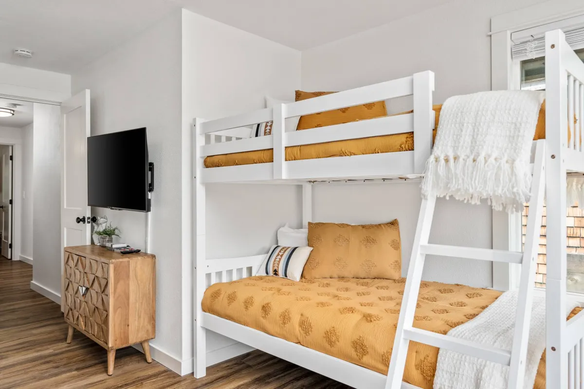 A playful bunk-bed room with a wooden dresser, television, and relaxed atmosphere perfect for cozy movie nights or gaming. The setup invites guests to unwind together, echoing the family-friendly, fun vibe described in the section.