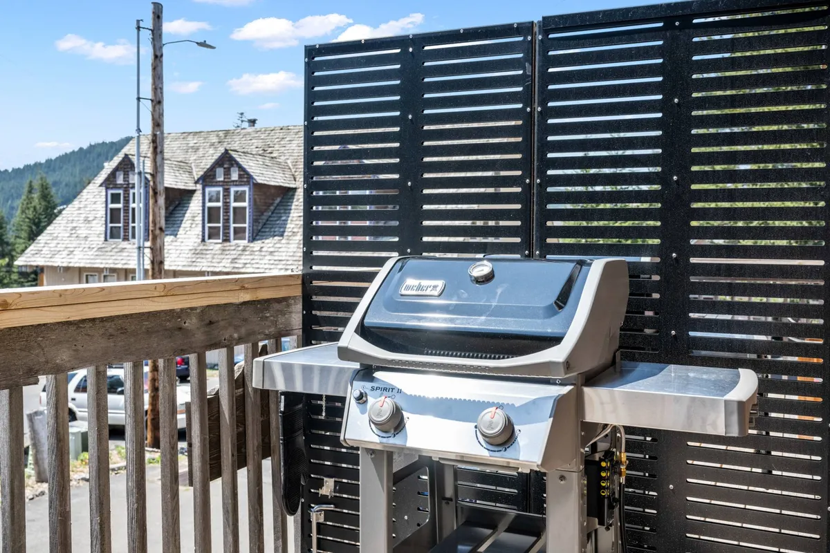 This exterior image showcases a wooden deck with a grill, surrounded by a sturdy railing and featuring the backdrop of the house. The outdoor setup communicates a welcoming and relaxed space for guests and their pets to enjoy the fresh mountain air, entertain, or simply unwind after an adventure-filled day.