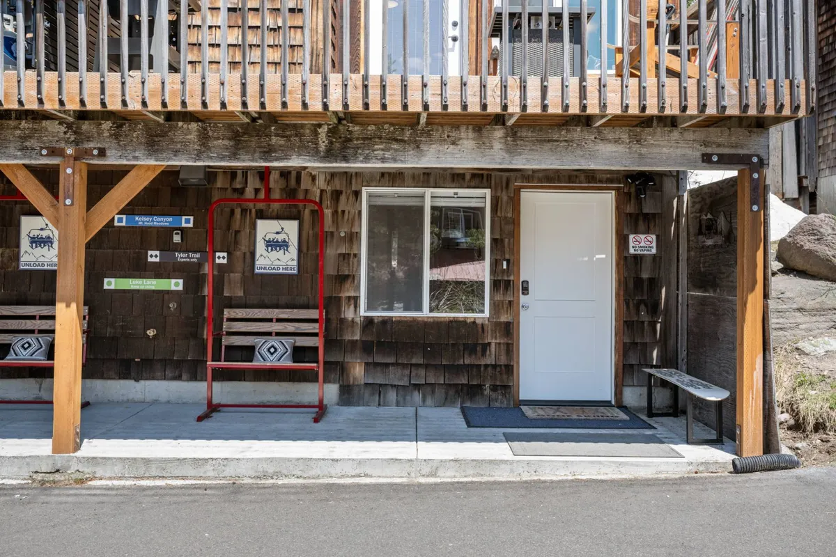 This image features the exterior front entryway of Nor Ski Haus B, showcasing the welcoming wooden entries, a cheerful red swing bench, and the front door. The area is inviting, with space for guests to relax outdoors and enjoy the neighborhood ambiance.