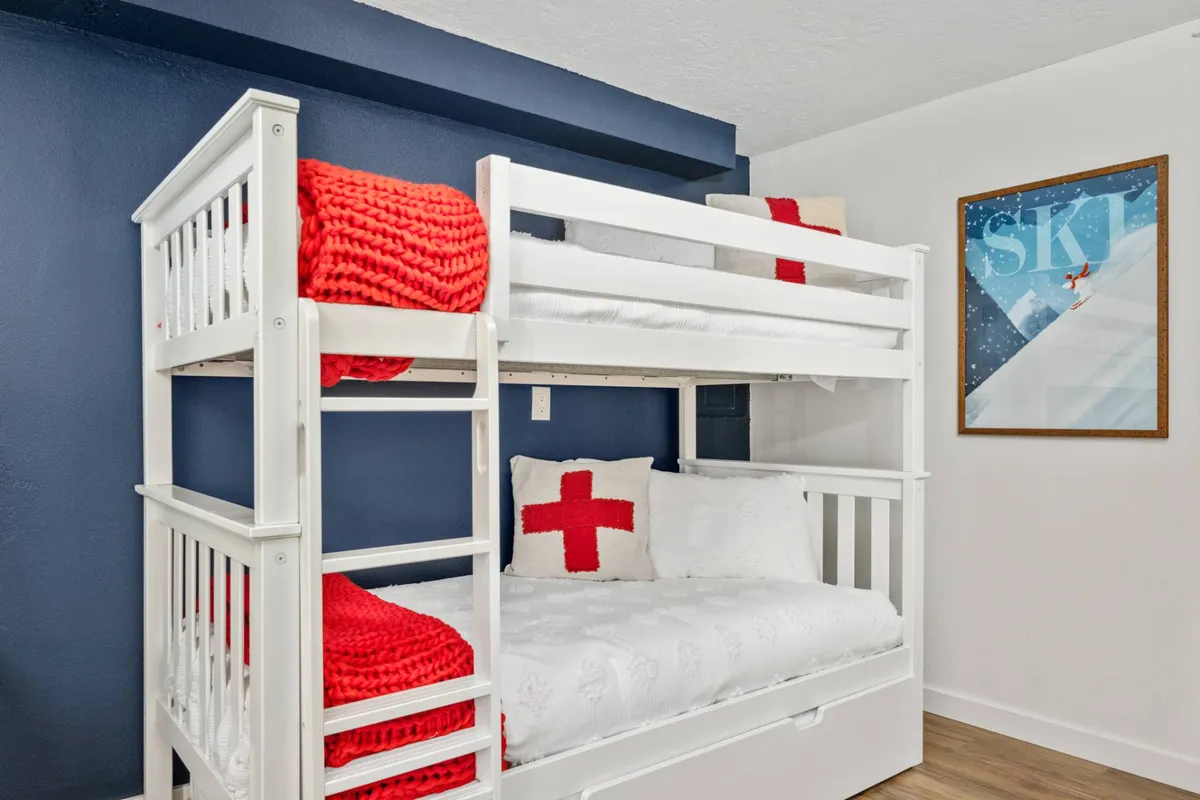 A cheerful, inviting bunk room with bold red blankets and a decorative pillow. Framed wall art adds a playful touch, and the atmosphere suggests shared stories or game nights after outdoor excursions.