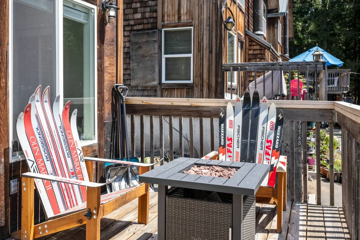A wooden deck with custom ski chairs, a fire pit, and lush surrounding greenery. The space is designed for socializing, relaxing, and transitioning easily between indoor and outdoor living, with nods to ski culture.