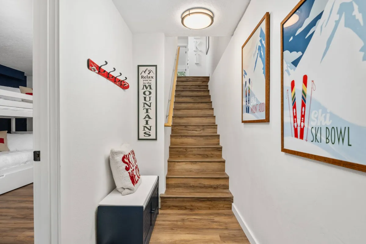 An interior space featuring a staircase with ski-themed artwork, a bench with a decorative pillow for sitting while putting on or taking off boots, and convenient coat hooks—ideal for organizing gear and outdoor attire.