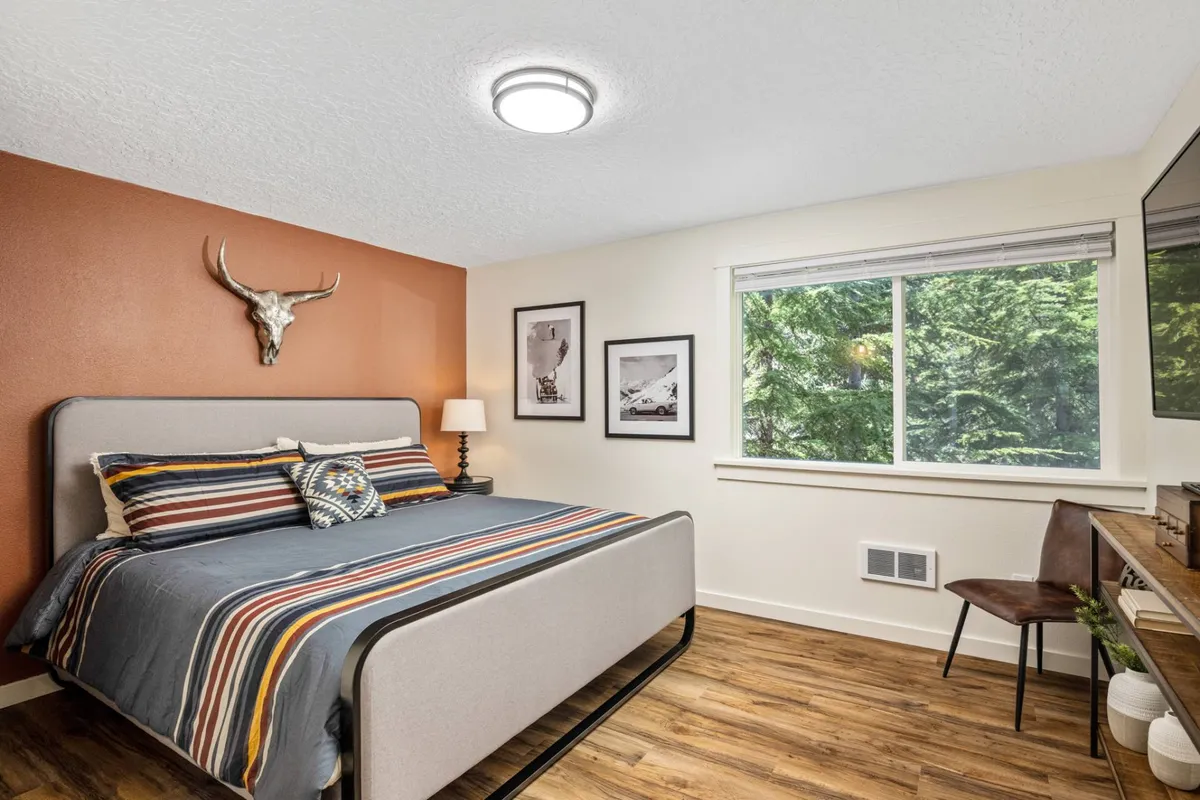 A serene bedroom with a plush bed, decorative wall art, and a large window offering views of the outdoors. The nightstand and distinctive horn decor add character, while the window hints at the peaceful mountain setting just outside.