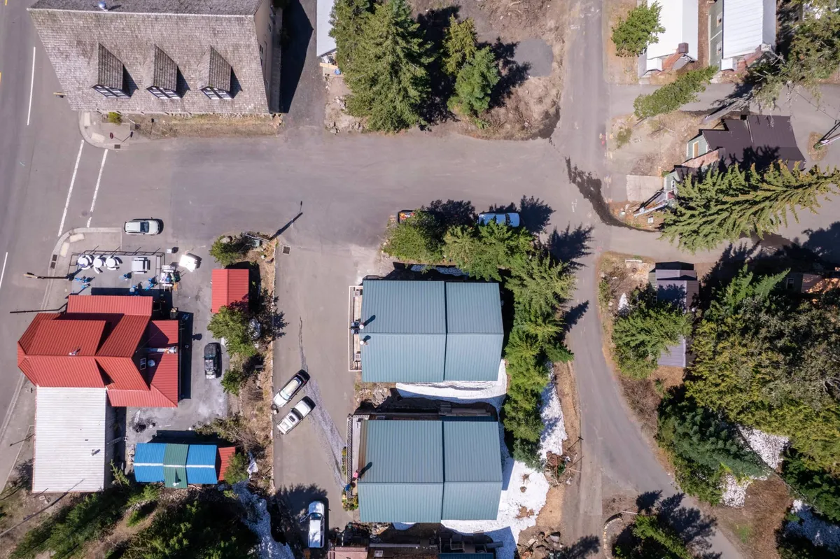 An inviting view of the surrounding neighborhood, featuring green buildings with distinctive red roofs, lots of tree coverage, and a central road intersection. People can be seen walking, suggesting community activity and proximity to local events or shops.
